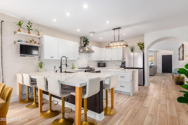 kitchen featuring a peninsula, arched walkways, stainless steel appliances, a kitchen bar, and wall chimney range hood