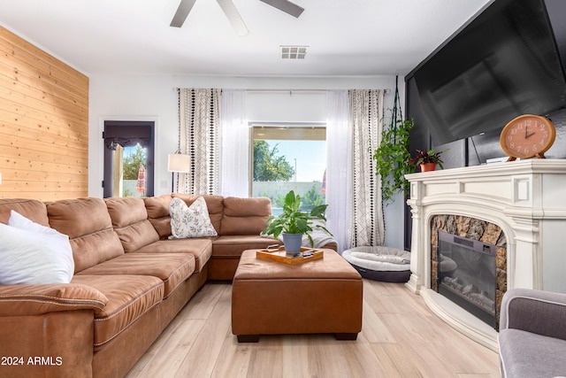 living room with a fireplace, light hardwood / wood-style flooring, ceiling fan, and wooden walls