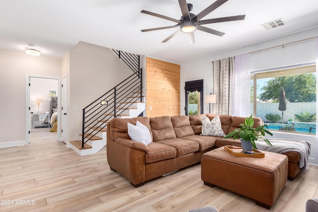 living room featuring visible vents, stairway, light wood finished floors, baseboards, and ceiling fan