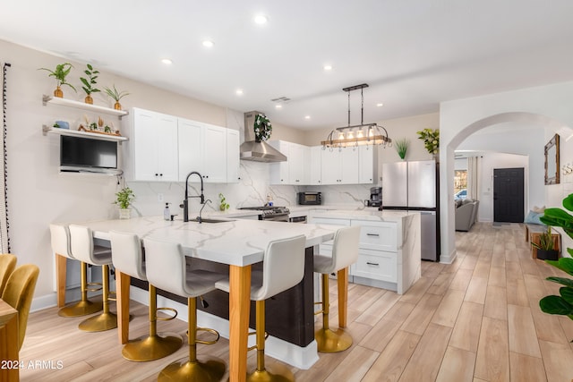 kitchen with wall chimney exhaust hood, light hardwood / wood-style flooring, appliances with stainless steel finishes, kitchen peninsula, and white cabinets