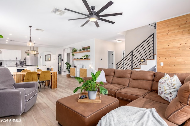 living room with visible vents, light wood-style flooring, ceiling fan with notable chandelier, and stairs