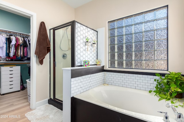 bathroom with a bath, a stall shower, a walk in closet, and wood finished floors