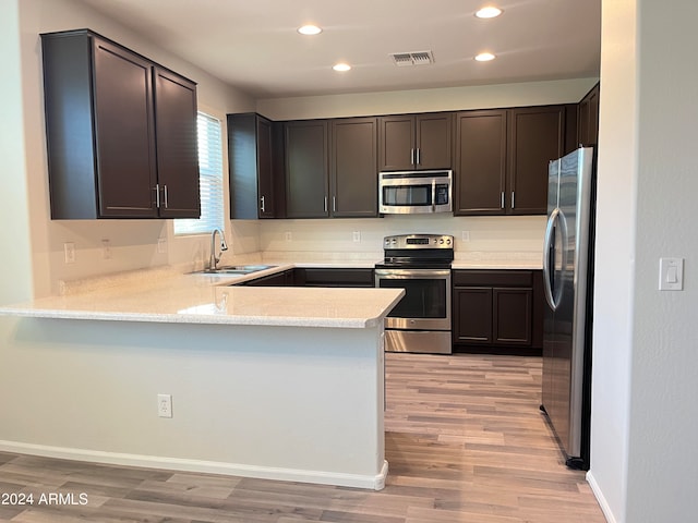 kitchen with kitchen peninsula, dark brown cabinets, sink, light wood-type flooring, and appliances with stainless steel finishes