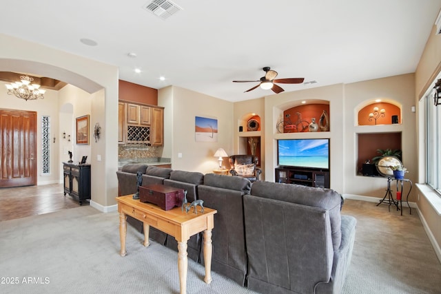 living room featuring light carpet, built in shelves, and ceiling fan with notable chandelier