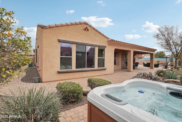 back of property with a hot tub, an outdoor living space, and a patio