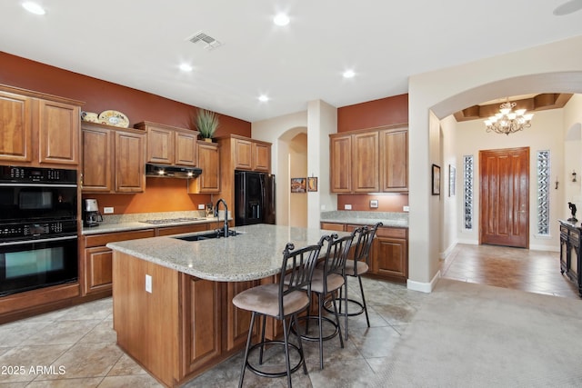 kitchen featuring black appliances, sink, a kitchen island with sink, light stone countertops, and light tile patterned floors