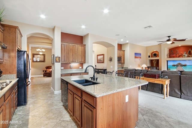 kitchen featuring a center island with sink, black appliances, sink, light stone counters, and ceiling fan with notable chandelier