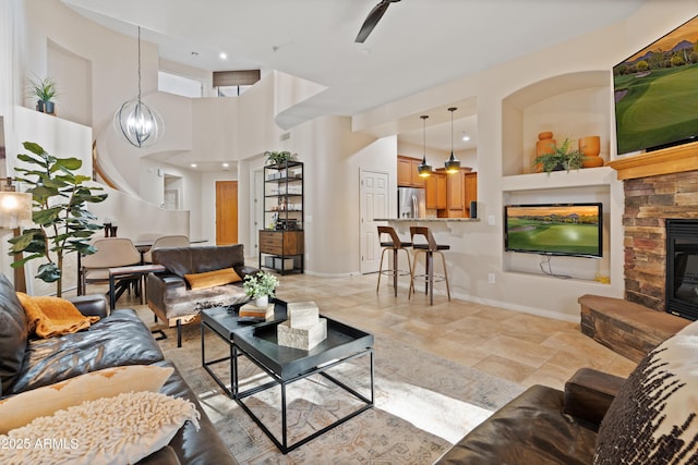 living room featuring ceiling fan with notable chandelier, a fireplace, and a towering ceiling