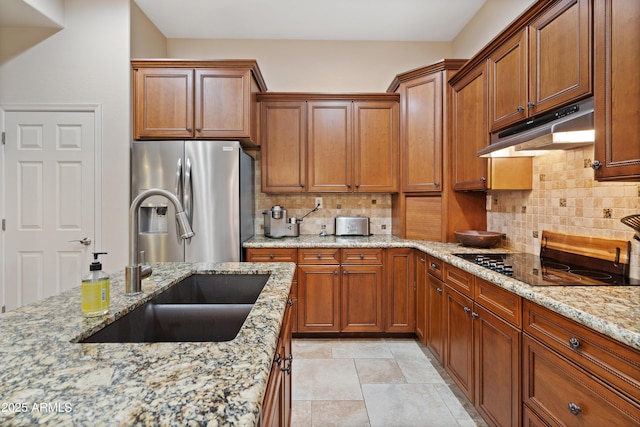 kitchen with sink, tasteful backsplash, light stone countertops, and stainless steel refrigerator with ice dispenser