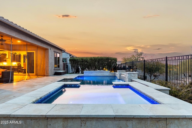 pool at dusk featuring a patio, pool water feature, and an in ground hot tub