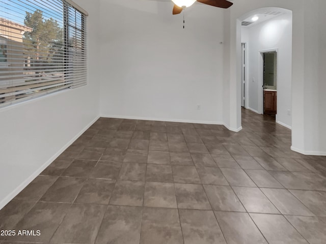 unfurnished room featuring baseboards, arched walkways, ceiling fan, and tile patterned floors