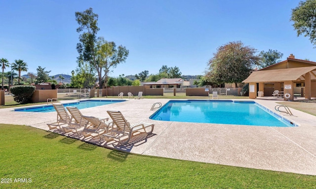 community pool with a patio area, a lawn, and fence