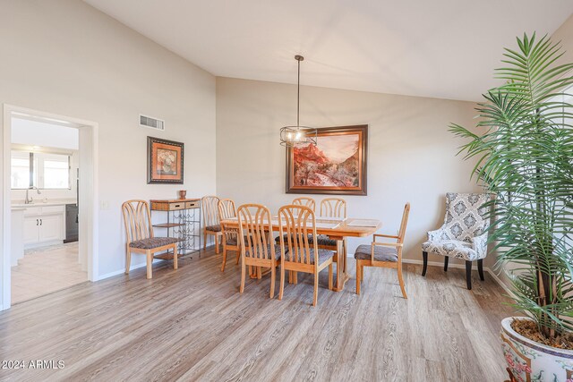 dining space with light hardwood / wood-style floors, sink, vaulted ceiling, and a notable chandelier