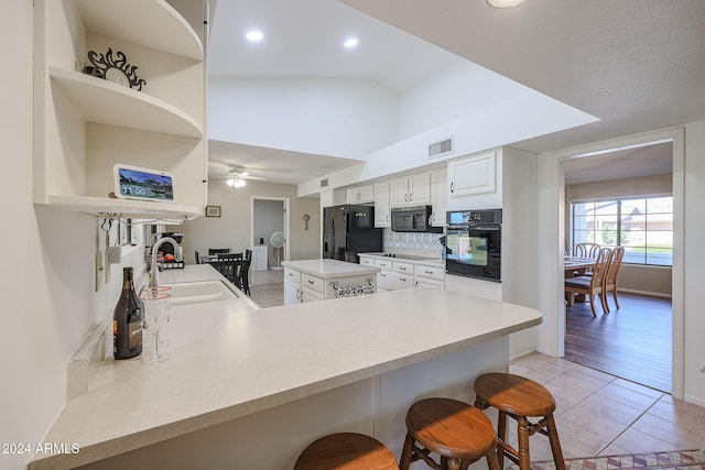 kitchen featuring black appliances, vaulted ceiling, white cabinets, kitchen peninsula, and a breakfast bar area