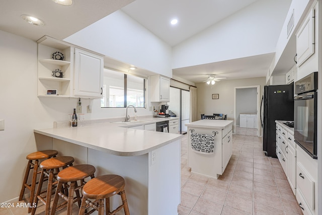 kitchen with black appliances, vaulted ceiling, a kitchen breakfast bar, white cabinets, and kitchen peninsula