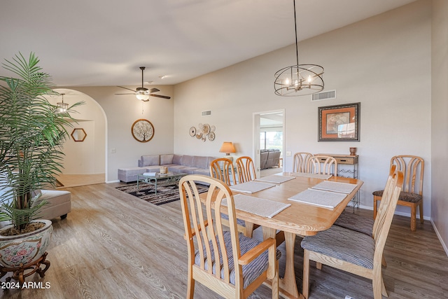 dining room with ceiling fan with notable chandelier, hardwood / wood-style flooring, and vaulted ceiling