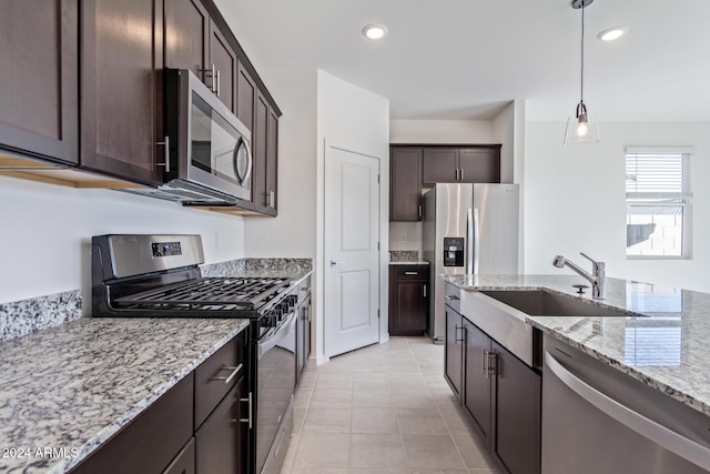 kitchen featuring pendant lighting, sink, light stone countertops, dark brown cabinetry, and stainless steel appliances