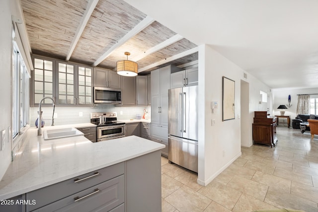 kitchen featuring a sink, appliances with stainless steel finishes, gray cabinets, decorative backsplash, and beamed ceiling