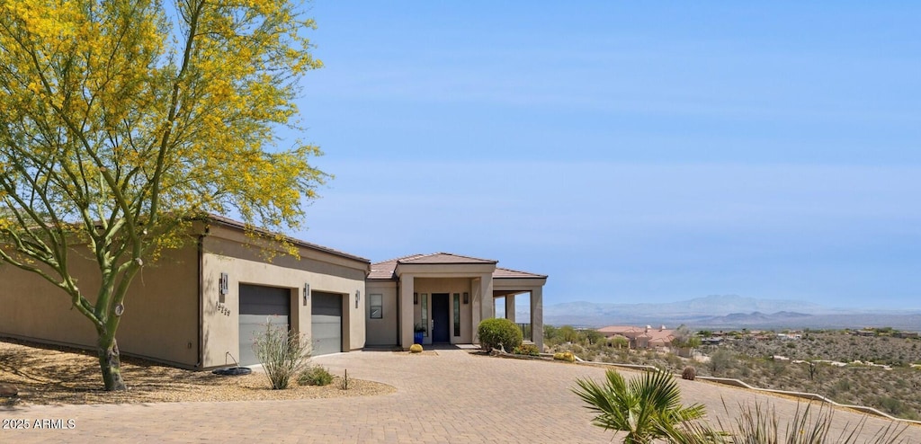 view of front facade with an attached garage, decorative driveway, a mountain view, and stucco siding