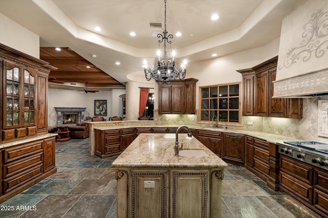 kitchen featuring stainless steel gas cooktop, sink, hanging light fixtures, a raised ceiling, and a kitchen island with sink