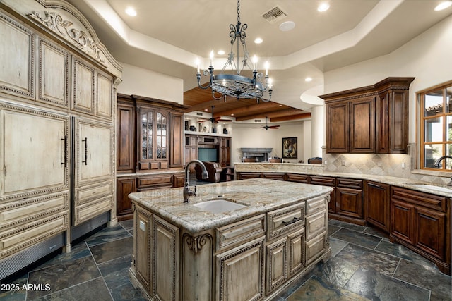 kitchen featuring sink, a raised ceiling, a kitchen island with sink, and decorative light fixtures