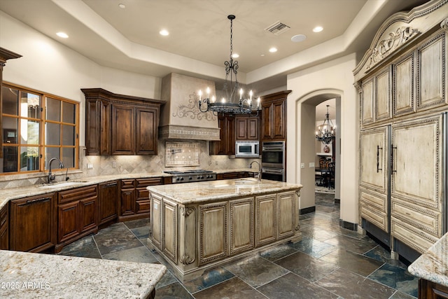 kitchen with sink, a kitchen island with sink, stainless steel appliances, a notable chandelier, and light stone countertops