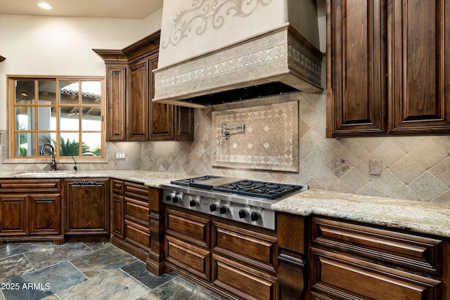 kitchen featuring stainless steel gas stovetop, sink, backsplash, custom exhaust hood, and light stone counters