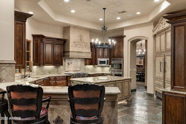 kitchen featuring sink, a center island with sink, custom range hood, pendant lighting, and stainless steel appliances