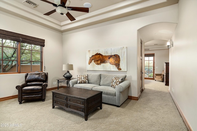 living room featuring ceiling fan, light colored carpet, and a raised ceiling