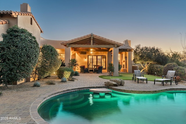 pool at dusk with an outdoor living space and a patio area