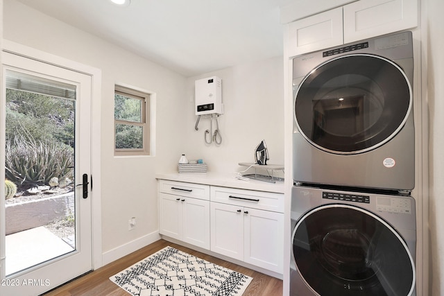 clothes washing area featuring cabinets, stacked washing maching and dryer, and light wood-type flooring