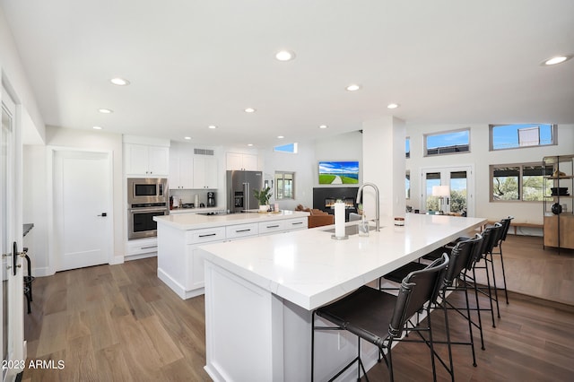 kitchen with appliances with stainless steel finishes, light hardwood / wood-style floors, white cabinetry, a center island with sink, and sink