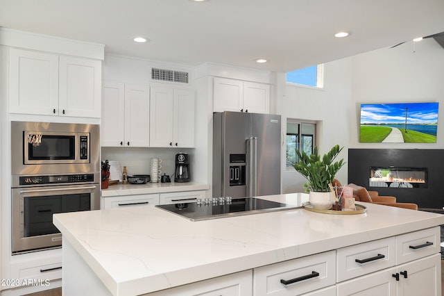 kitchen featuring light stone countertops, stainless steel appliances, white cabinetry, and a kitchen island