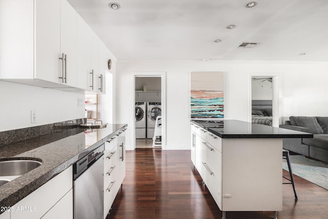 kitchen featuring a kitchen bar, washer and clothes dryer, stainless steel dishwasher, visible vents, and dark wood-type flooring