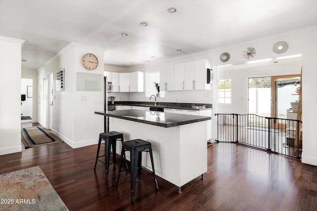 kitchen featuring crown molding, white cabinetry, dark wood-style flooring, and a kitchen breakfast bar