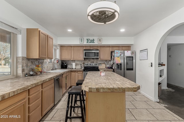 kitchen featuring a kitchen bar, a sink, light countertops, stainless steel appliances, and decorative backsplash