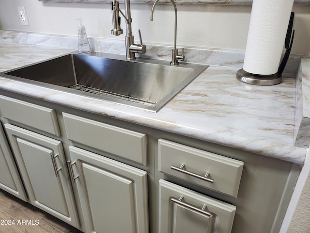 room details with sink, light stone counters, wood-type flooring, and gray cabinetry