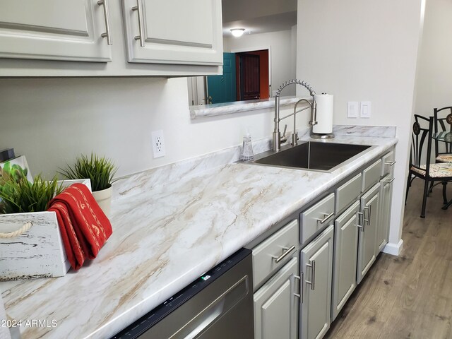 kitchen featuring dishwashing machine, hardwood / wood-style flooring, sink, light stone counters, and gray cabinetry