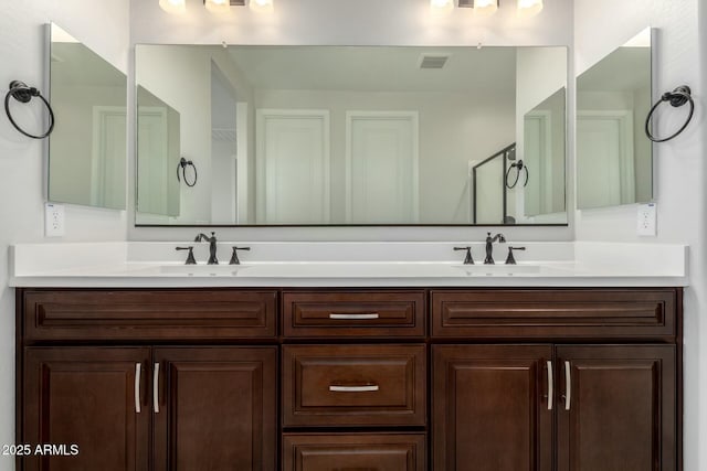 full bathroom with double vanity, an enclosed shower, visible vents, and a sink