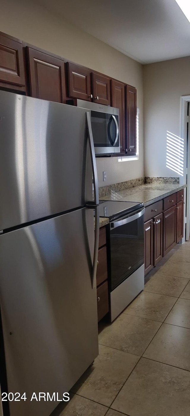 kitchen featuring dark brown cabinetry, light tile patterned flooring, and appliances with stainless steel finishes