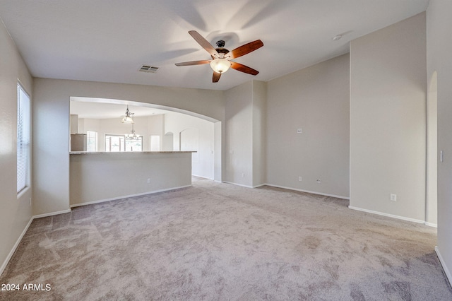 unfurnished living room featuring ceiling fan with notable chandelier and light carpet