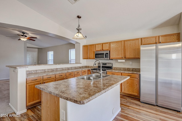 kitchen with lofted ceiling, sink, appliances with stainless steel finishes, a kitchen island with sink, and decorative light fixtures