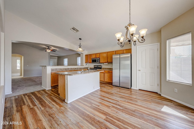 kitchen with decorative light fixtures, vaulted ceiling, an island with sink, and appliances with stainless steel finishes