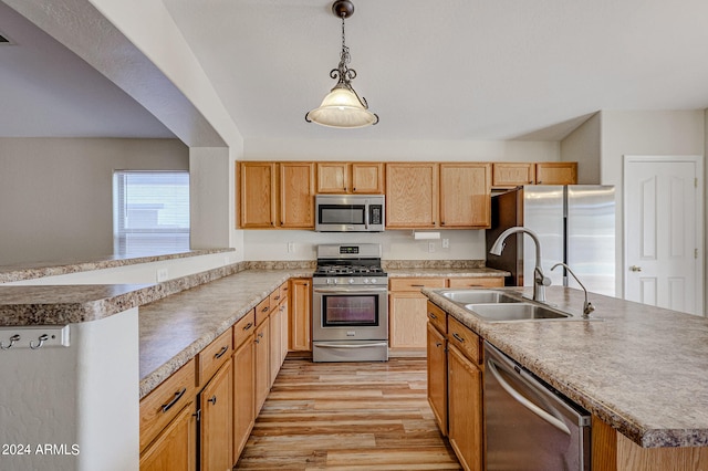 kitchen with appliances with stainless steel finishes, pendant lighting, sink, a kitchen island with sink, and light wood-type flooring