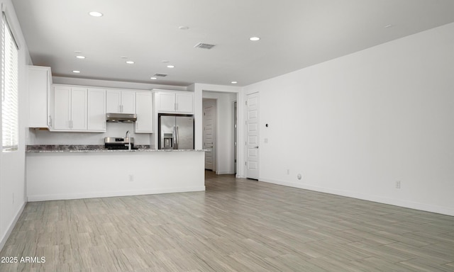 kitchen featuring white cabinetry, light wood-type flooring, dark stone countertops, kitchen peninsula, and stainless steel appliances