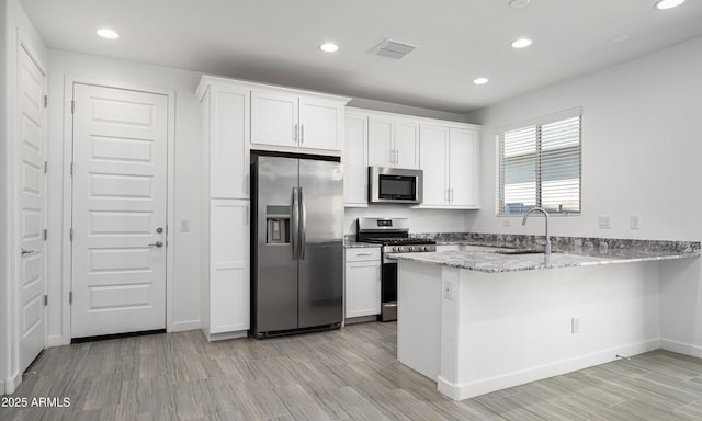 kitchen featuring sink, stainless steel appliances, light stone counters, white cabinets, and kitchen peninsula