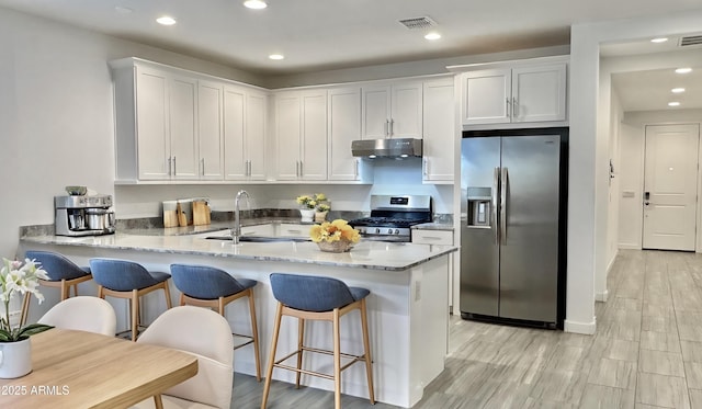 kitchen featuring appliances with stainless steel finishes, white cabinetry, sink, light stone counters, and kitchen peninsula