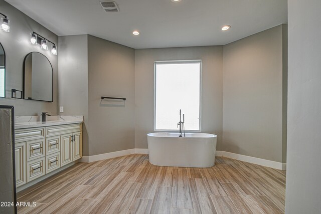 bathroom with hardwood / wood-style floors, a bathing tub, double vanity, and a healthy amount of sunlight