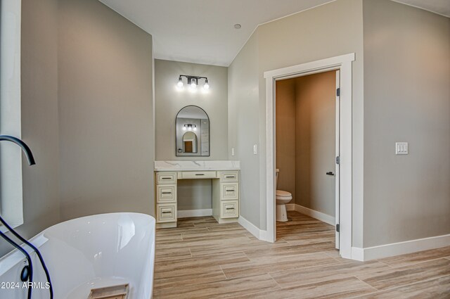 bathroom featuring toilet, large vanity, a washtub, and vaulted ceiling