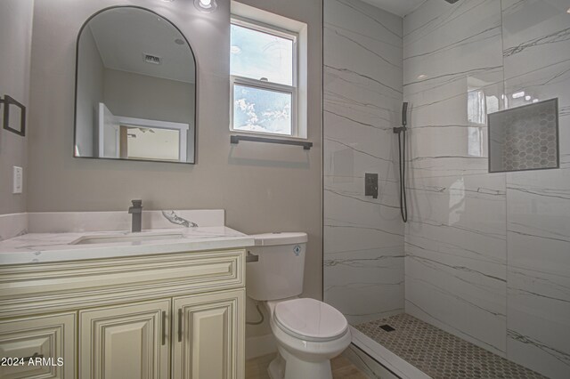 bathroom with toilet, a tile shower, and vanity